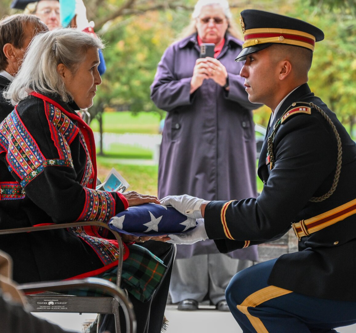 Ann Washburn Lord, the fifth great-granddaughter of Private Oliver Barrett, receives an American flag in his honor from Capt. Eric Sampson of the New York National Guard Honor Guard during military honors for the dedication of a memorial stone for Barrett at the Saratoga National Cemetery Oct. 19, 2022.  Barrett volunteered as a Minuteman and died serving under the 10th Massachusetts Regiment in the Battle of Saratoga on Oct. 7, 1777, at 51 years of age.