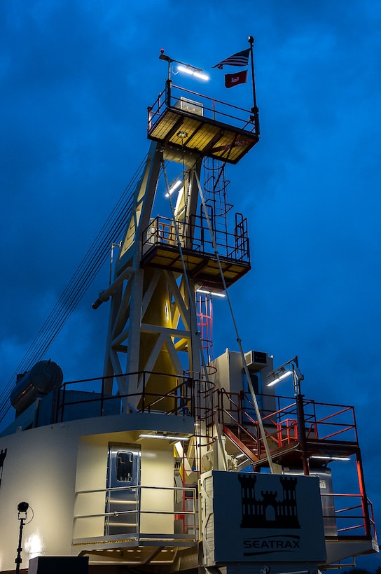 Derrickboat illuminated by the lights on the vessel in the early blue morning sky.