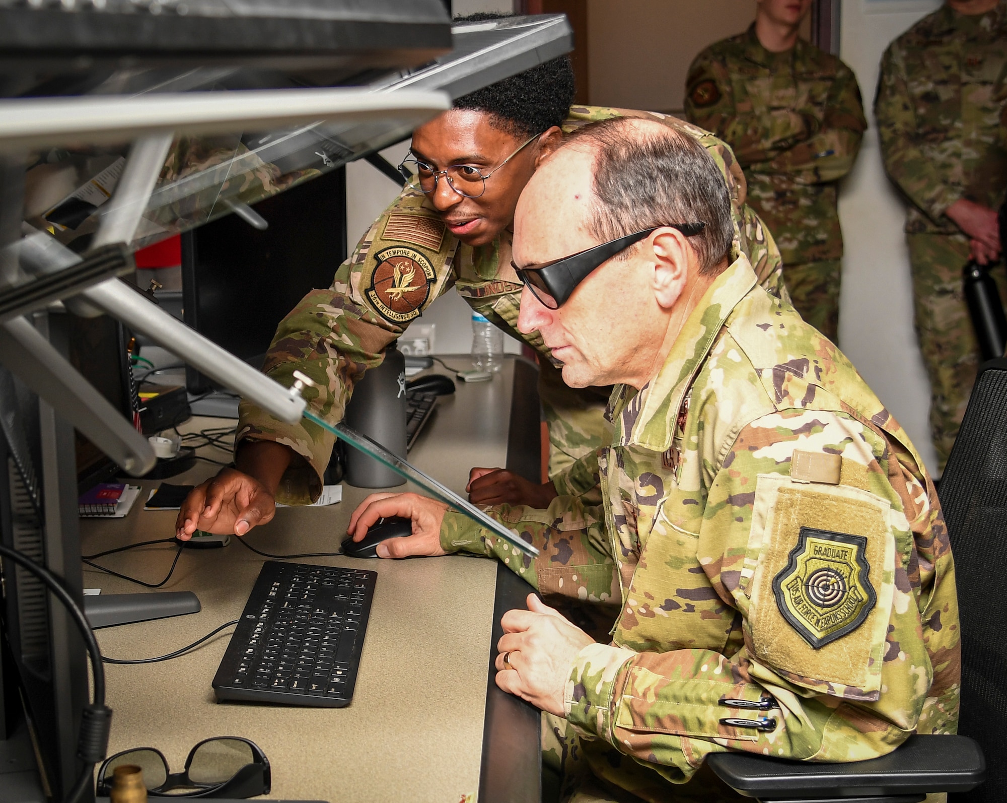 Airman demonstrates how to use a 3D monitor to another individual.