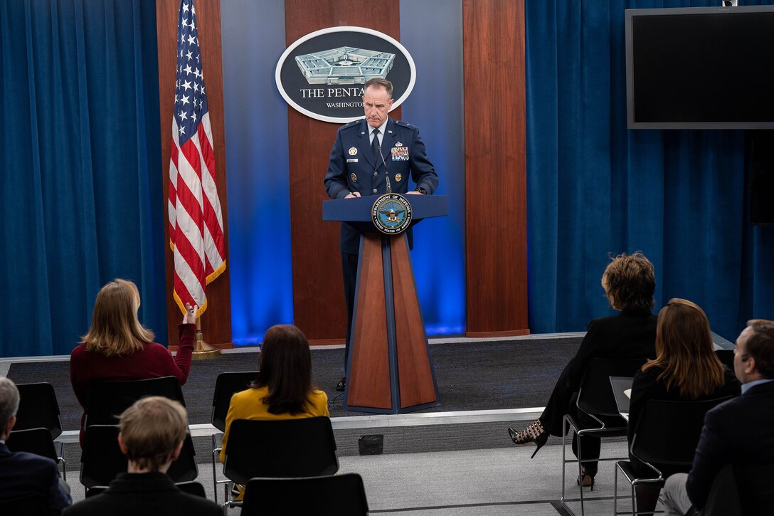 An airman stands at a lectern and listens to a seated audience member.