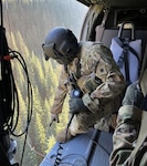 Spc. Nicholas Ehrenheim, a Black Hawk crew member with1st Battalion, 168th General Support Aviation, Washington Army National Guard, points down to an opening in a heavily wooded area near Leavenworth, Wash., Oct. 15, 2022. The Guard aircrew rescued a hiker who sustained a chest injury.