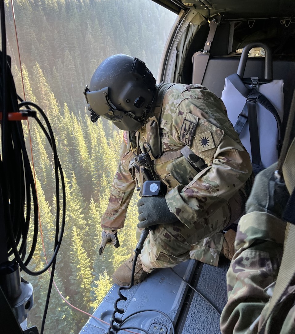 Spc. Nicholas Ehrenheim, a Black Hawk crew member with1st Battalion, 168th General Support Aviation, Washington Army National Guard, points down to an opening in a heavily wooded area near Leavenworth, Wash., Oct. 15, 2022. The Guard aircrew rescued a hiker who sustained a chest injury.