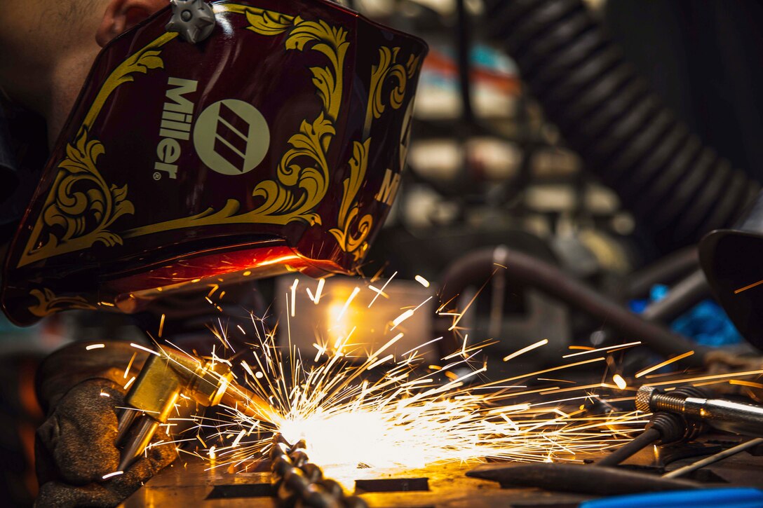 Sparks fly as a sailor welds metal aboard a ship.