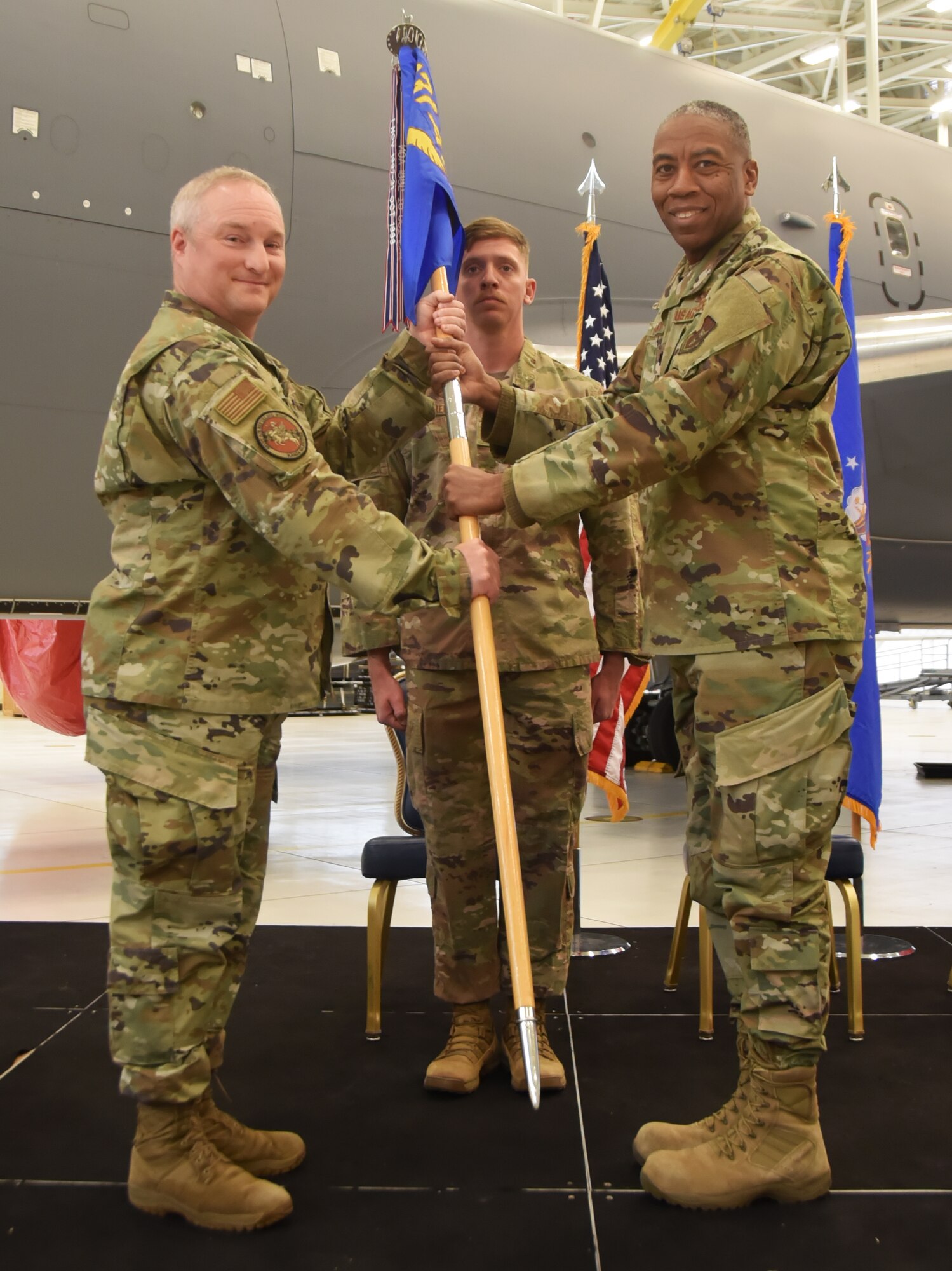 Left and right. Col. Mark Basler takes the guidon to Lt. Col. Kelvin Haywood while standing on podium.