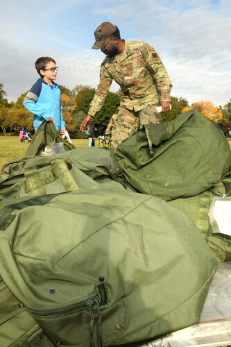 Man in camouflage uniform speaks with young boy near a pile of deployment bags