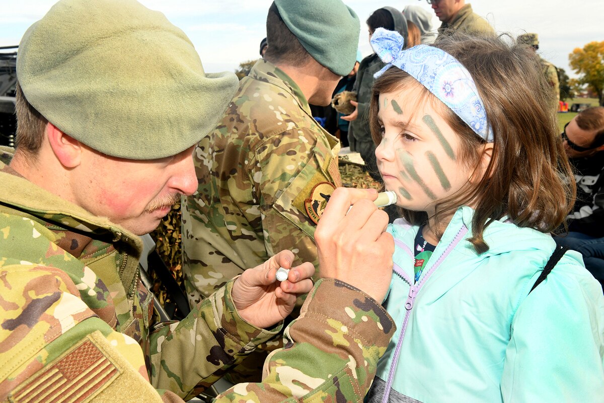 Uniformed man applies camouflage face paint to young girl's face