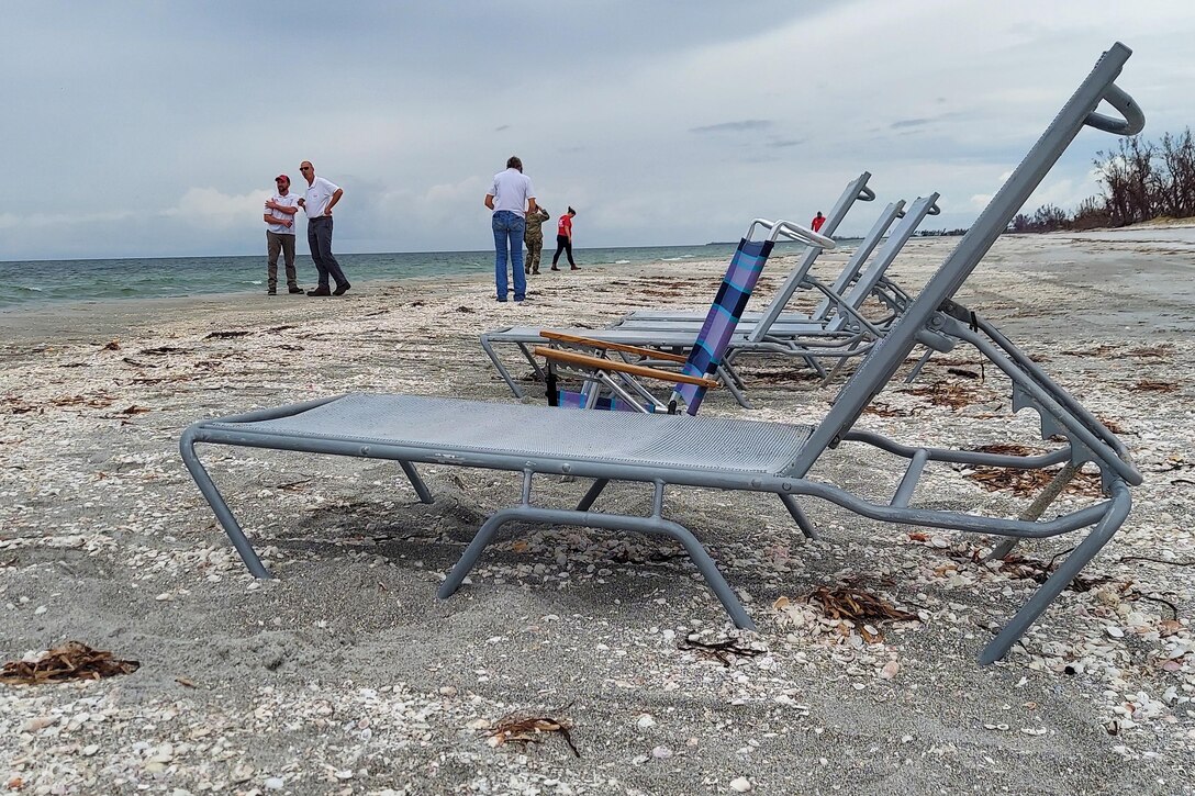 A group of engineers survey hurricane damage on a beach with lounge chairs in the foreground.