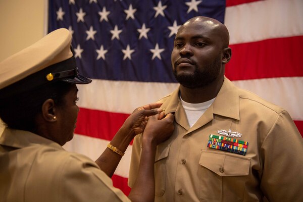 NAVAL STATION NORFOLK (Oct. 21, 2022) A chief petty officer mentor pins Chief Culinary Specialist Prince Kudalor’s anchors during the Naval Surface Force Atlantic chief petty officer pinning ceremony onboard Naval Station Norfolk, Oct. 21, 2022. Nine Sailors received their gold-fouled anchors during the ceremony. (U.S. Navy photo by Mass Communication Specialist 1st Class Jacob Milham)