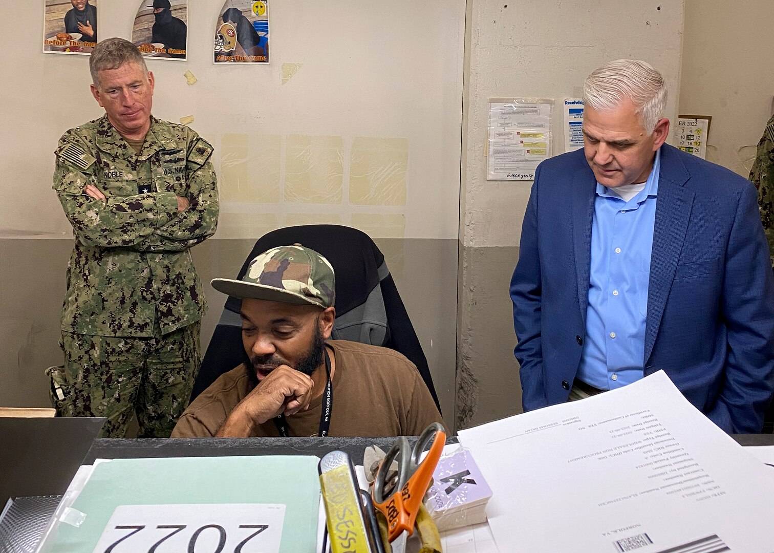 Two men look over a man's shoulder.