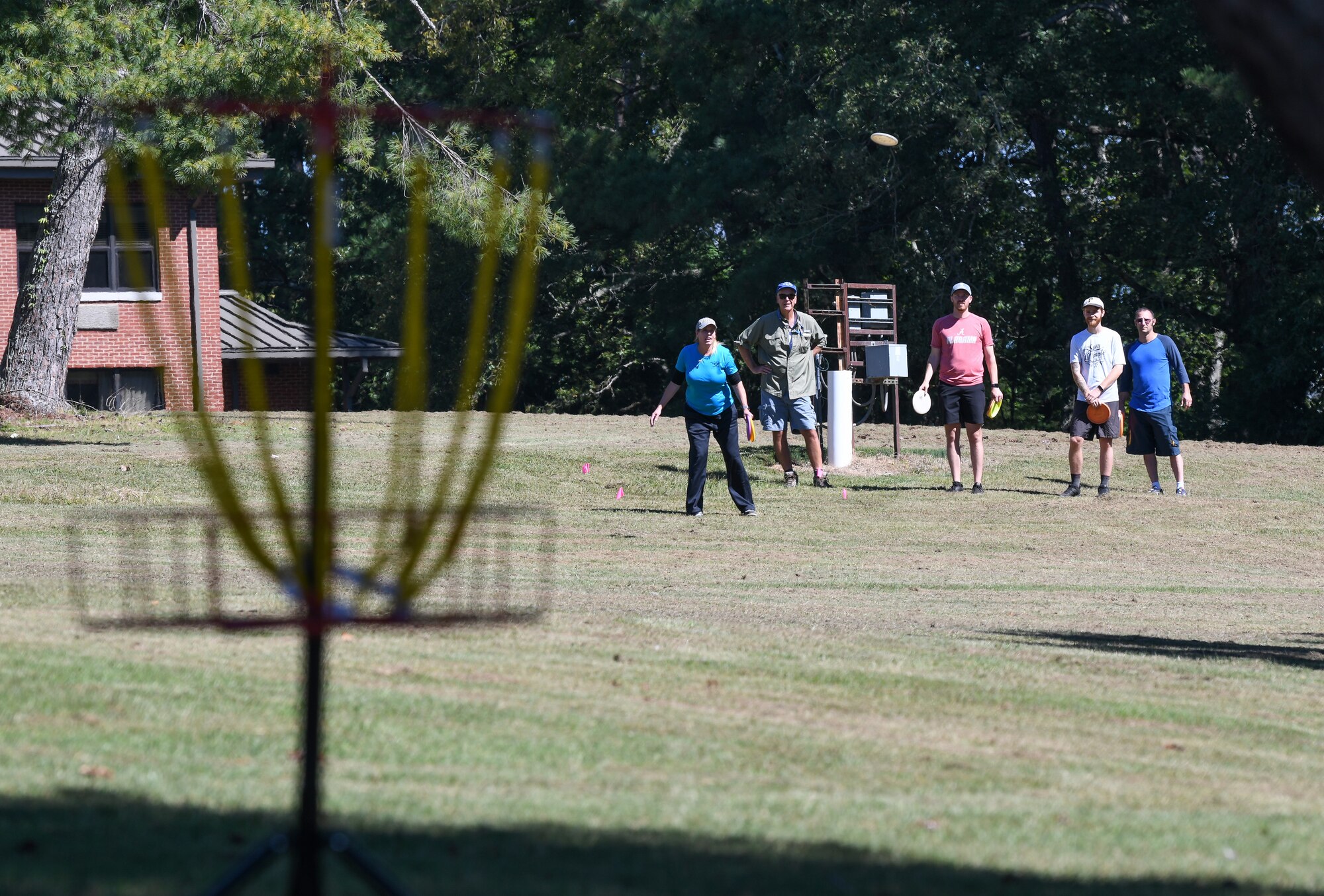 Woman watches her disc fly while playing disc golf as others wait their turn