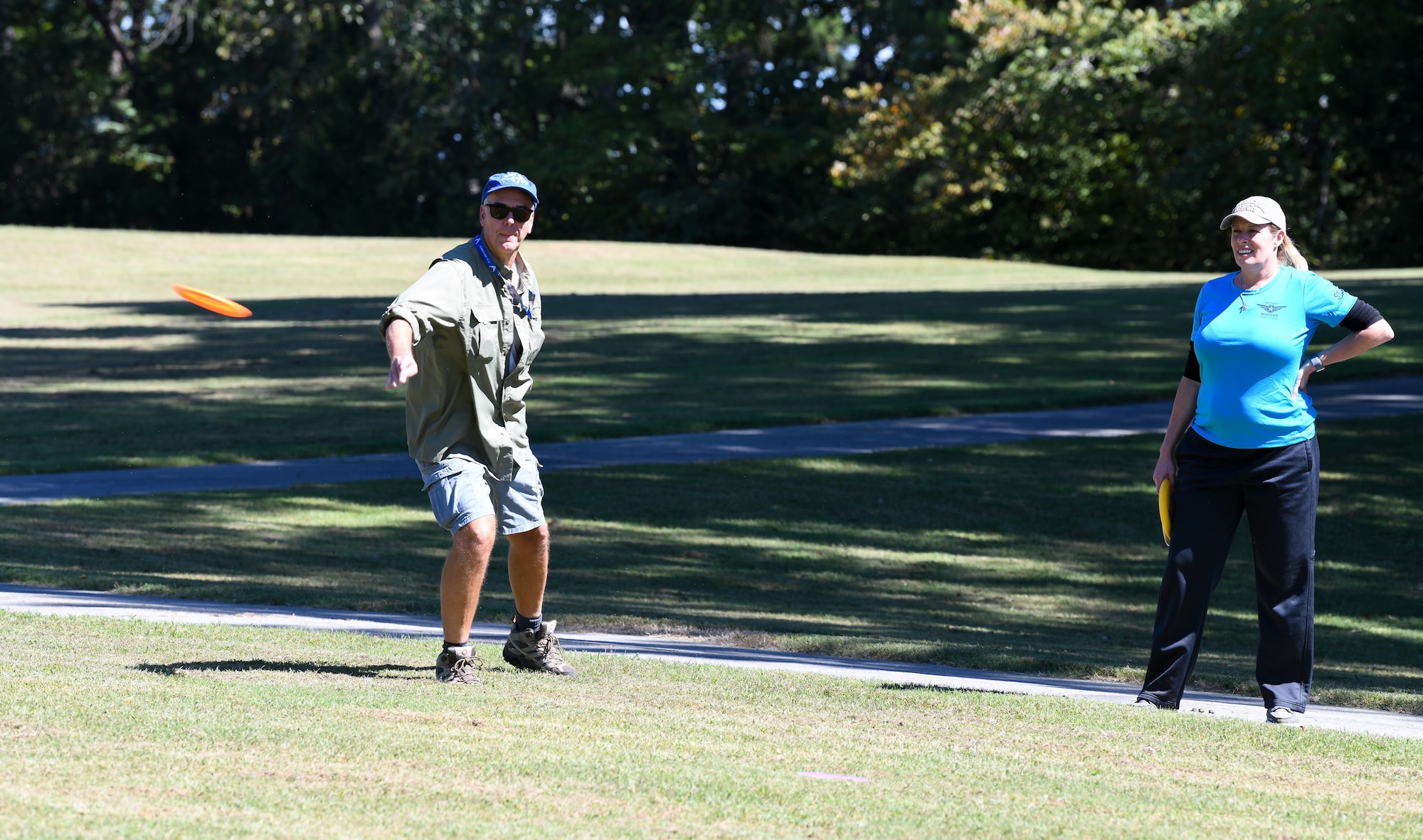 Man throws disc while playing disc golf as woman watches