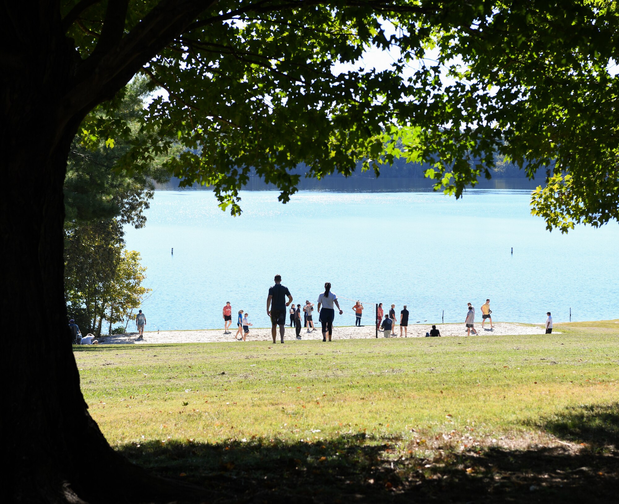 Two people walking toward sand volleyball court and lake where others play volleyball