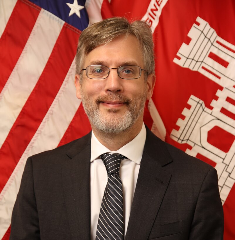 Image of male in front of USACE and American flags