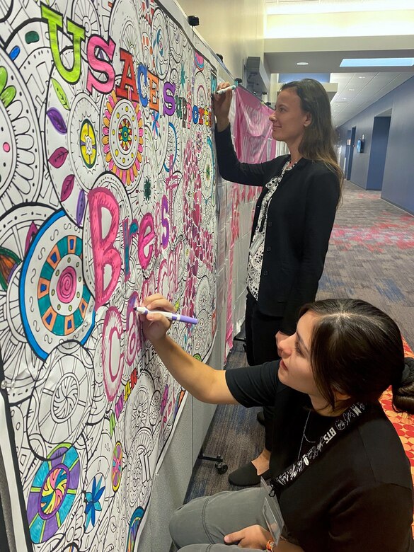 Alex Chestnut, chemist, and Sabrina Duncan, environmental engineer, color a Breast Cancer Awareness Month poster during a training break October 12, 2022. The poster, hung up in the hallway at Huntsville Center during the entire month of October, is one of many ways the Safety Office and breast cancer survivor Tara Payne are raising awareness about the importance of screenings and early detection. (Photo by Kristen Bergeson)