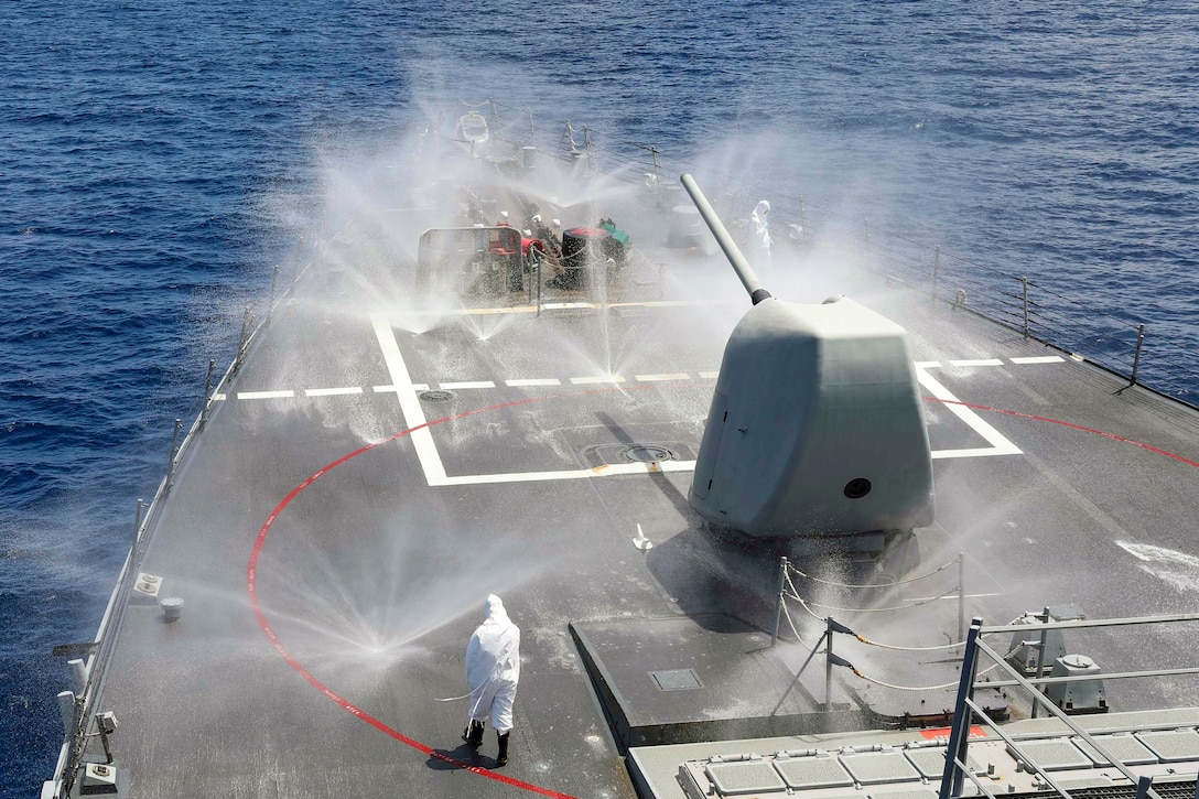 Sailors wearing protective gear wash down the front of a ship.