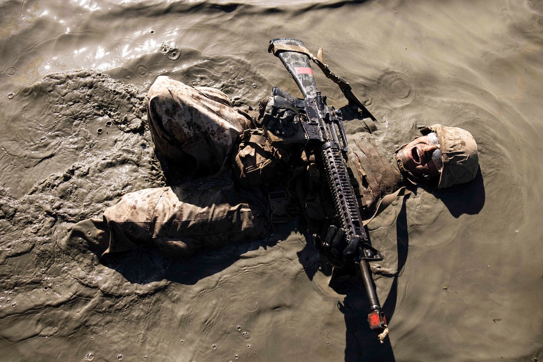 A Marine lays in mud while holding a weapon.
