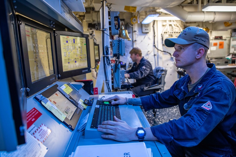 Sailors sit at a command console aboard a ship.
