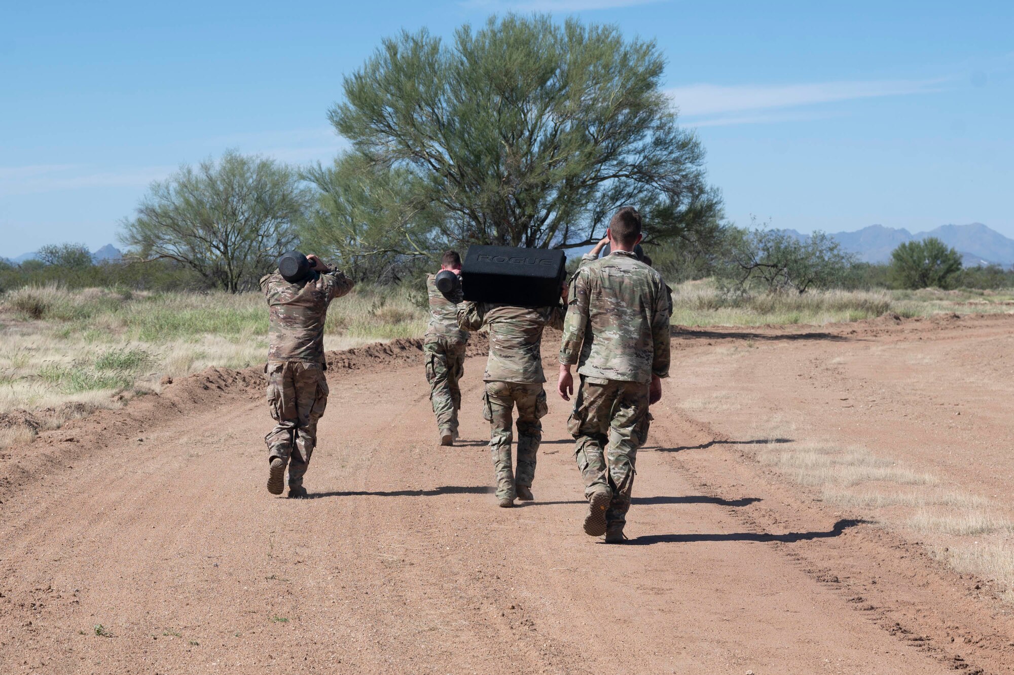 Pictured above are people walking carrying weights down a dirt trail.