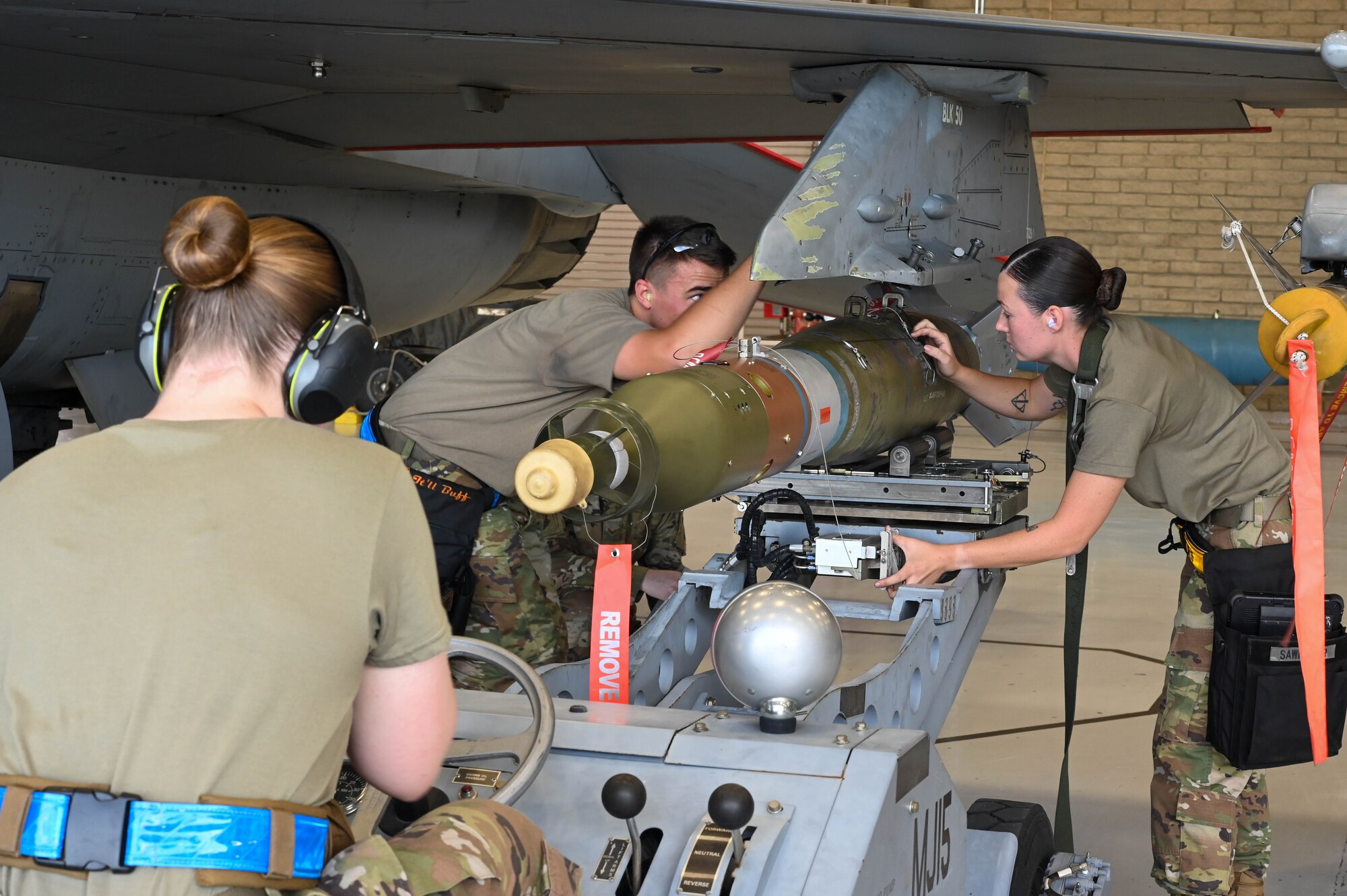 U.S. Air Force Staff Sgt. Janey Sawmiller (right), Senior Airman Ross Hall (center), and Airman 1st Class Theresa Calvert (left), 309th Aircraft Maintenance Unit maintainers, use a weapons jammer to load a GBU-12 Paveway II during a weapons load competition, Oct. 7, 2022, at Luke Air Force Base, Arizona.
