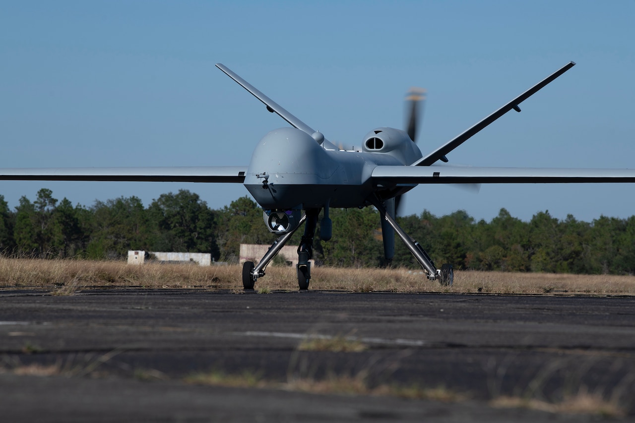 An unmanned aircraft sits on tarmac in large field.