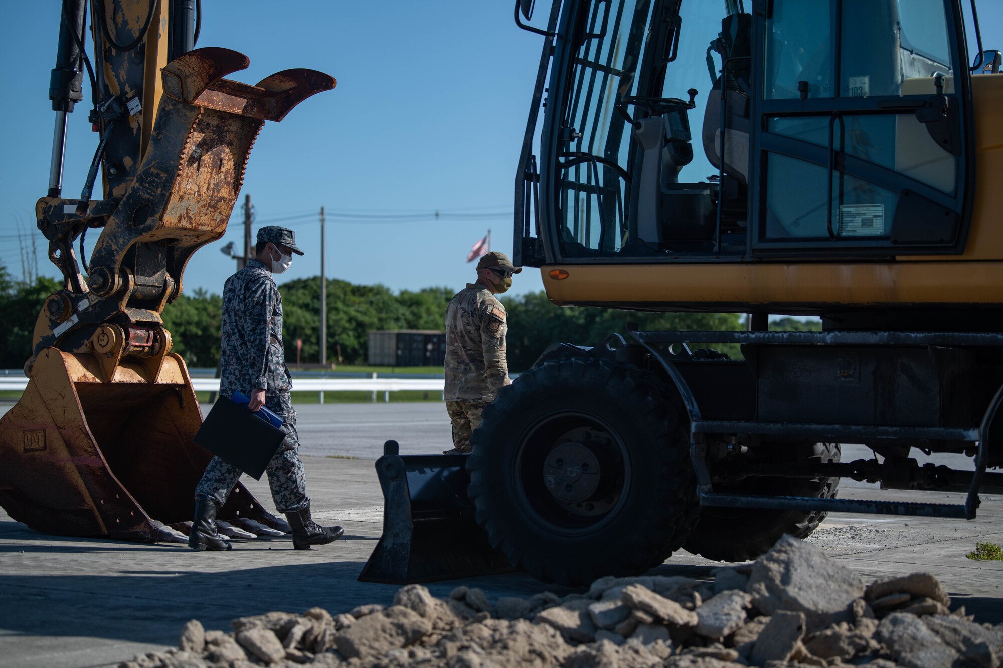 Military members walk around an excavator.