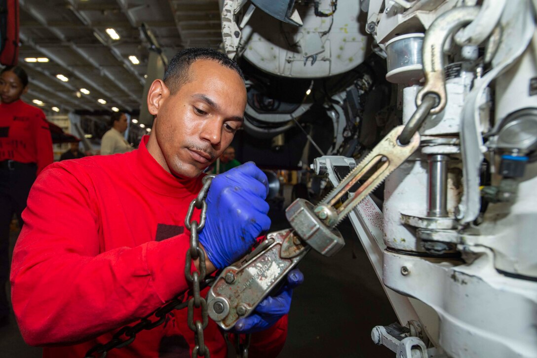 A sailor wearing gloves removes chains from an aircraft.