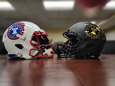 a white football helmets sits on a table facing a black football helmet