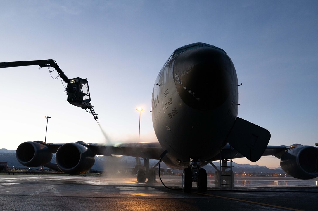 An airman sprays a chemical on the wing of a  large plane.