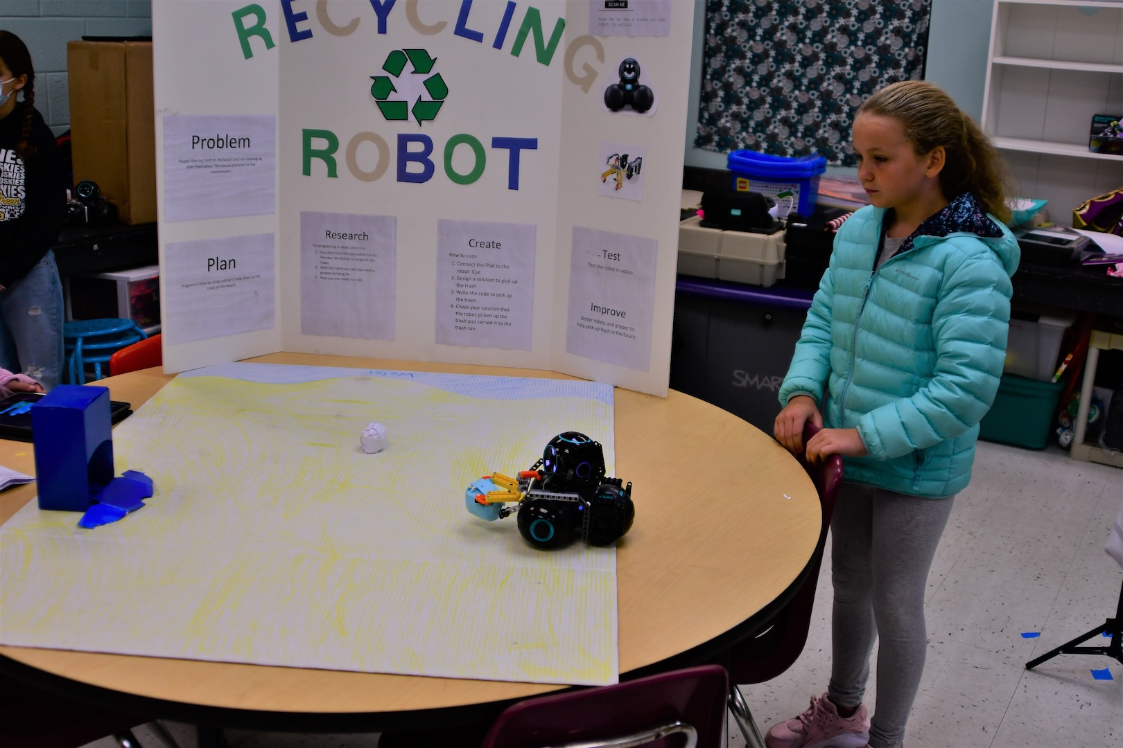 IMAGE: Bowling Green Elementary School fifth-grader Hayden Lambert looks on as the robot she helped create with classmate Kacie Hupp-Polla picks up trash and later empties it into a makeshift receptacle during the school’s STEM Fair on Oct. 13.