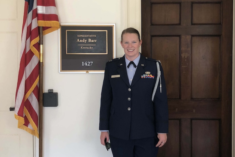 A woman stands in front of a door and plaque.