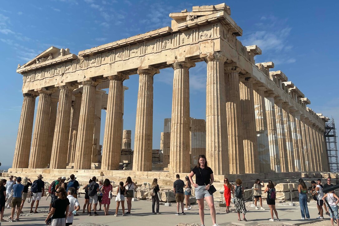 A woman poses for a photo in front of an ancient building made of columns.