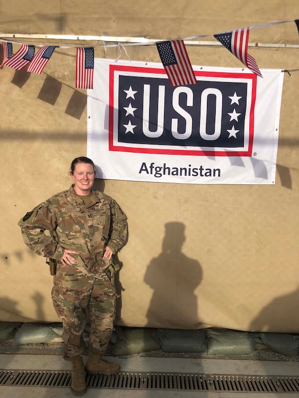 A woman poses for a photo in front of a USO banner.