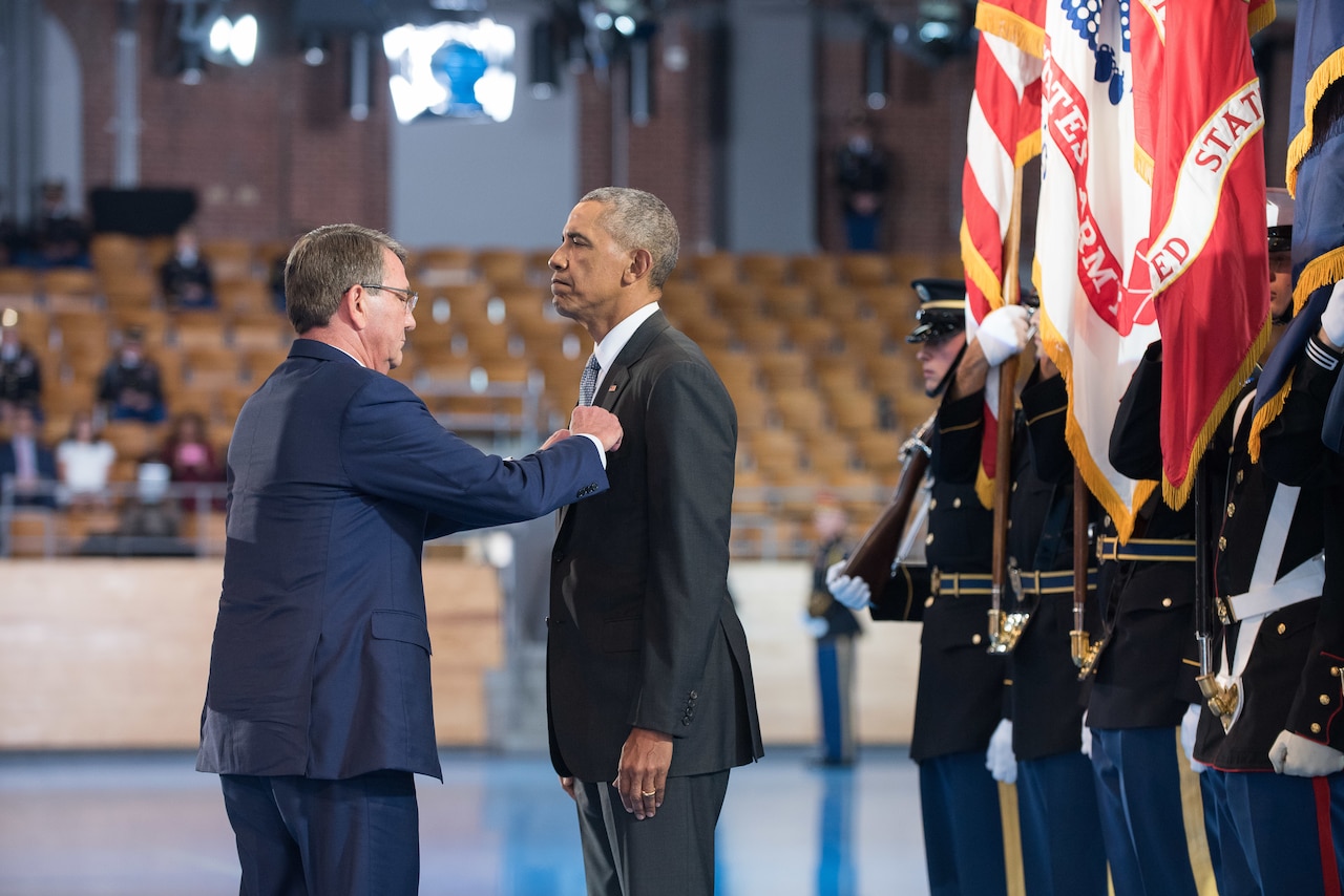 One man pins something to the lapel of another man as they stand opposite one another.