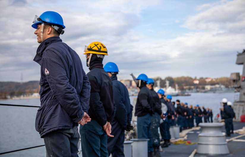 Sailors face seaward on the deck of a ship.