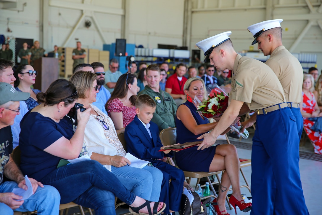 Two Marines hand flowers and a gift to two military family members in a group of audience members.