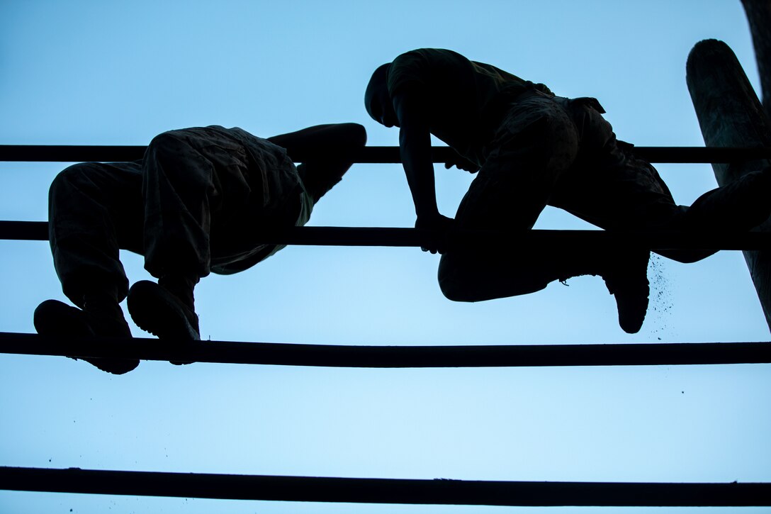 Two Marine Corps recruits balance on ropes all seen in silhouette.