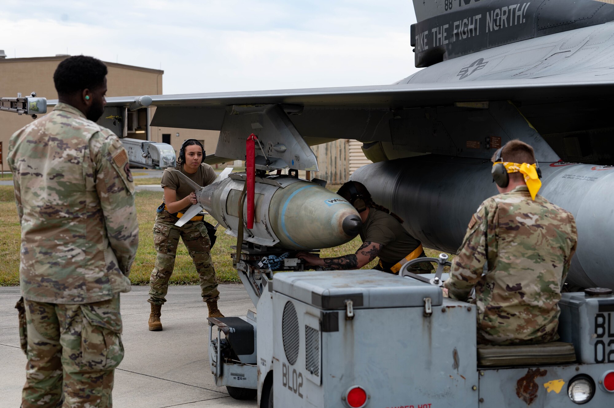 80th Fighter Generation Squadron weapons load crew members, guide a GBU-38 bomb