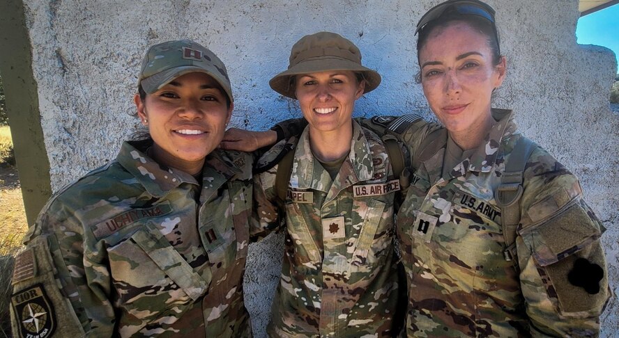 Three Airmen stand next to each other with arms wrapped around each other's shoulders.