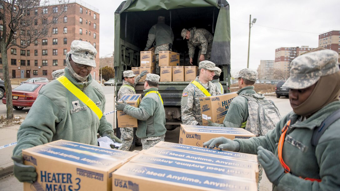 Service members pass boxes of supplies toward the back of a large military truck.