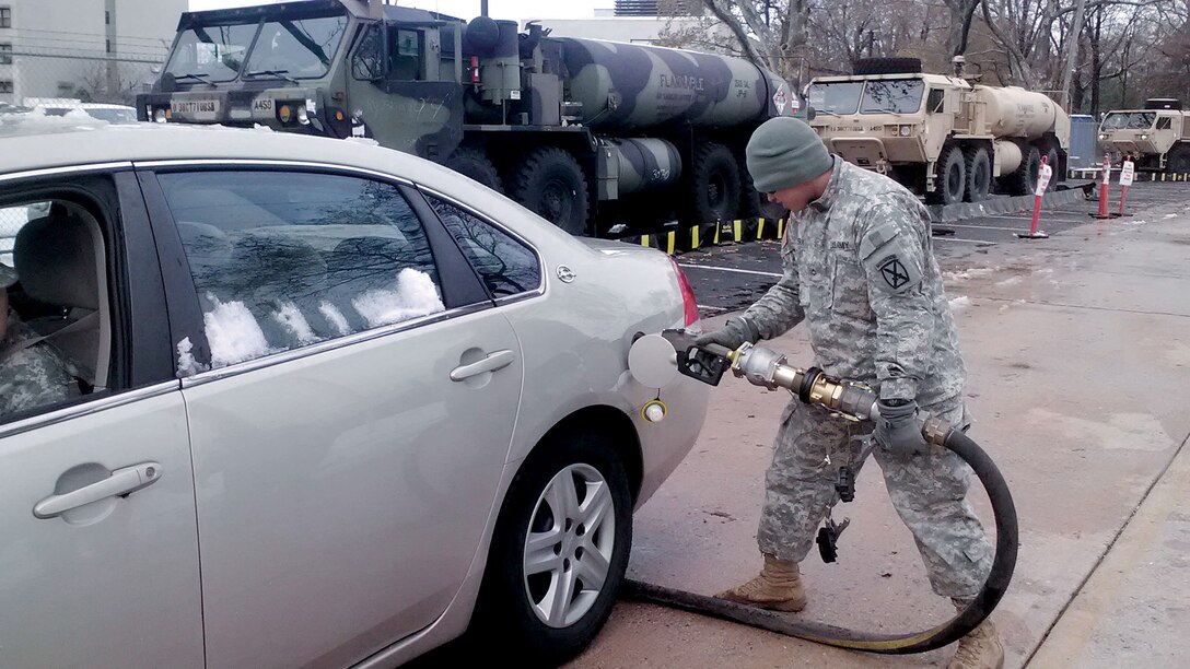 A service member pumps gas into a parked, snow-spattered car.