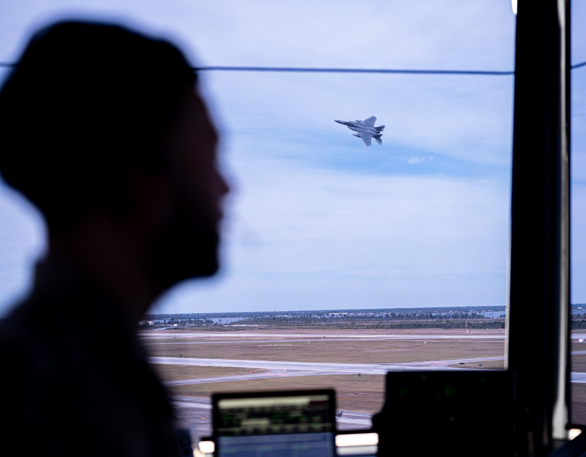 The shadow of an Airmans head is shown as a jet flies behind him