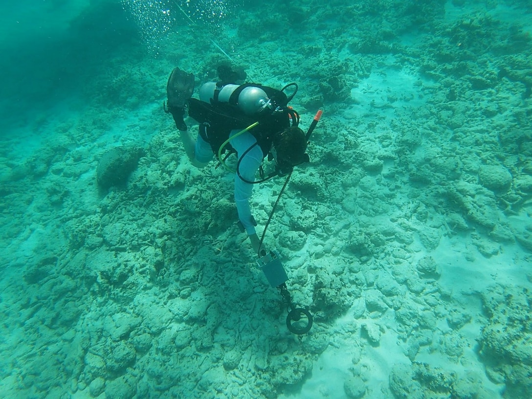 George Schwarz (NHHC) conducts a metal detector survey over a wreck site. Divers can be deployed with tools, like metal detectors, to assist in identifying or pinpointing iron objects. Some objects become overgrown with marine life and are difficult identify with the naked eye. If the object is buried, more exact location data will assist future research efforts.
