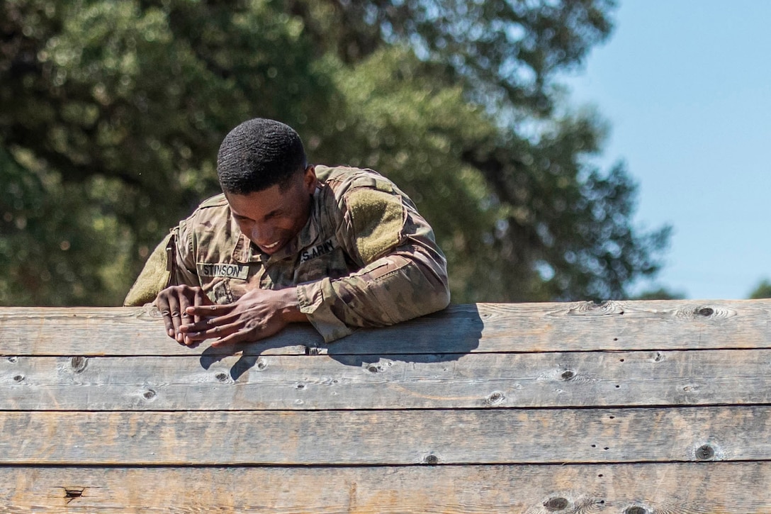 A soldier grimaces as he climbs over a high fence.