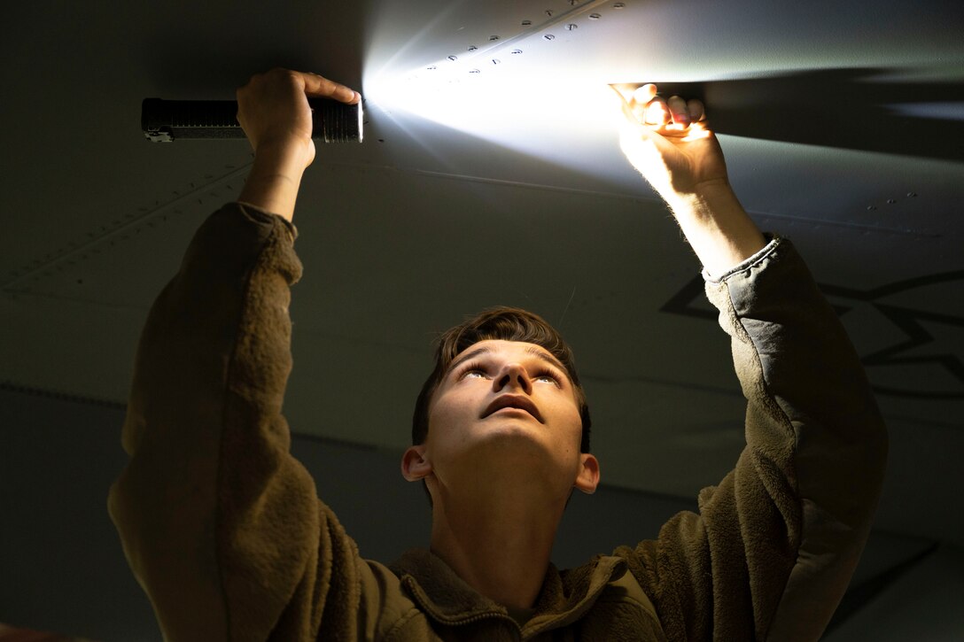 An airman uses a flashlight on an aircraft in the dark.