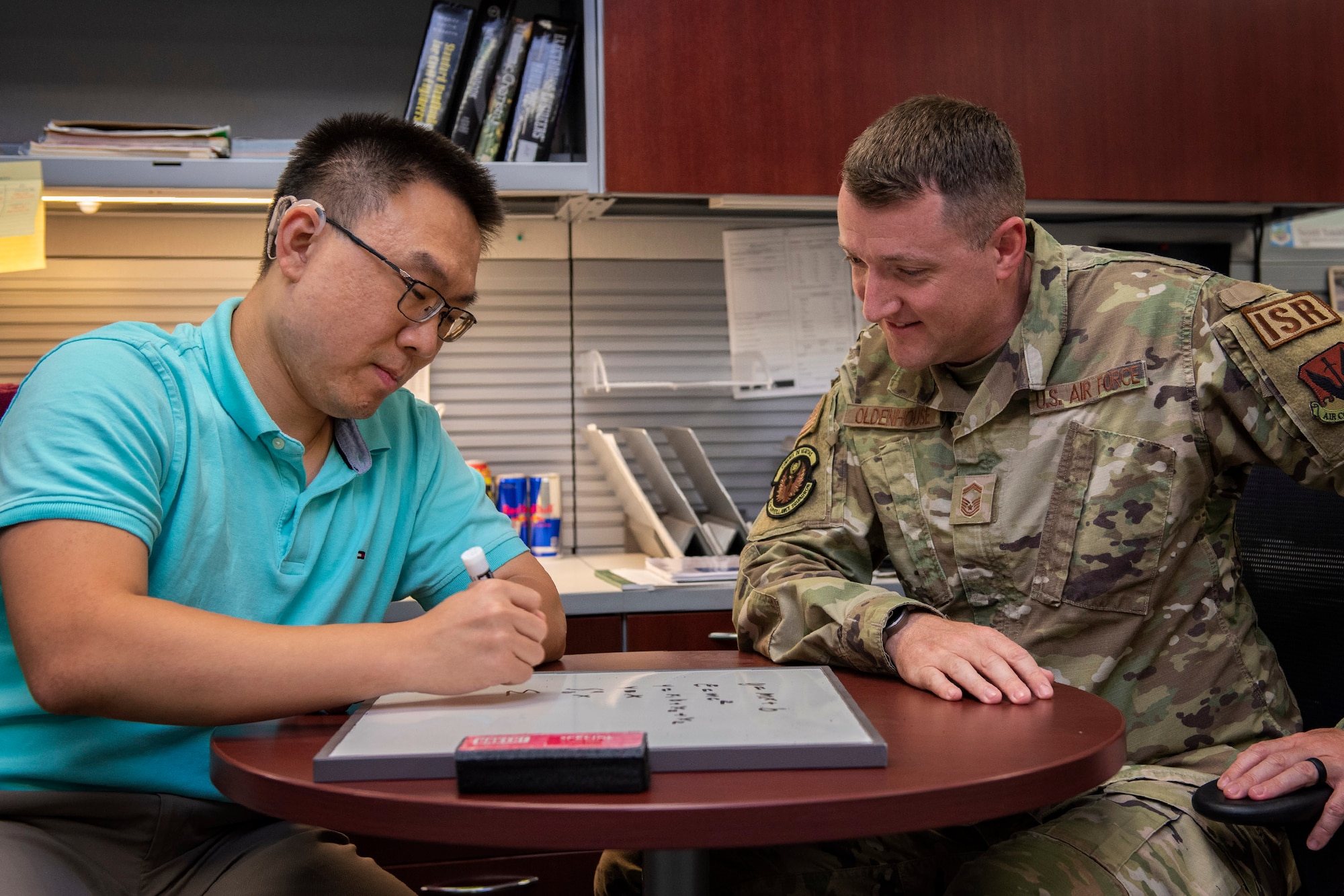 Le Chen, a statistician with the 21st Surveillance Squadron at Patrick Space Force Base, Fla., communicates with Senior Master Sgt. David M. Oldenhouse, 21st SURS Senior Enlisted Leader, using a white board and dry erase marker.  Chen is a hearing-impaired employee at the Air Force Technical Applications Center and uses a variety of methods to communicate with his coworkers.  (U.S. Air Force photo by Matthew S. Jurgens.)