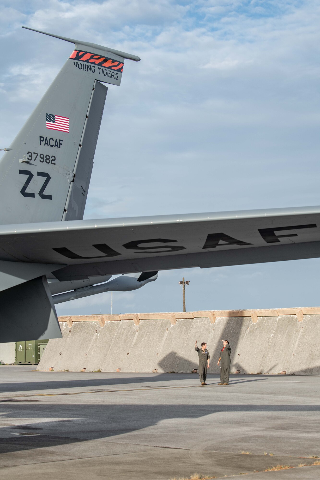 Two pilots inspect the tail of their refueling jet
