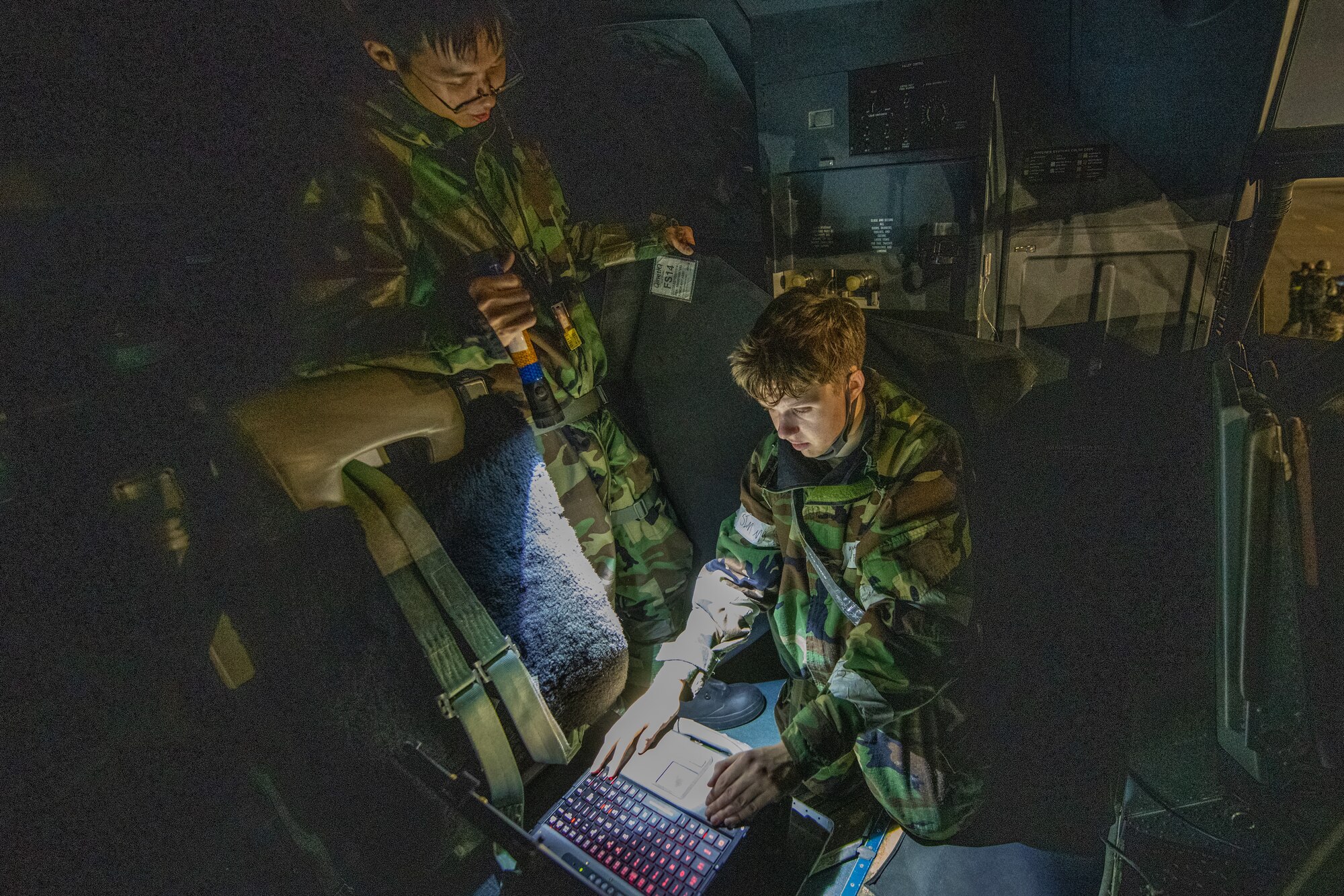 teo airmen in protective suits work on a plane in the dark