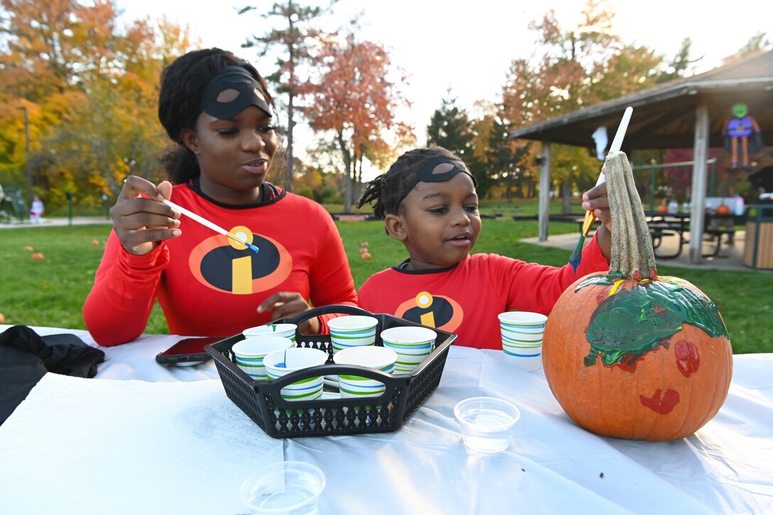 A mother and son sit at a table and paint a pumpkin.