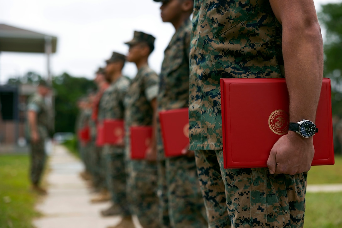 Marines line up in formation at a promotion ceremony holding their certificates.
