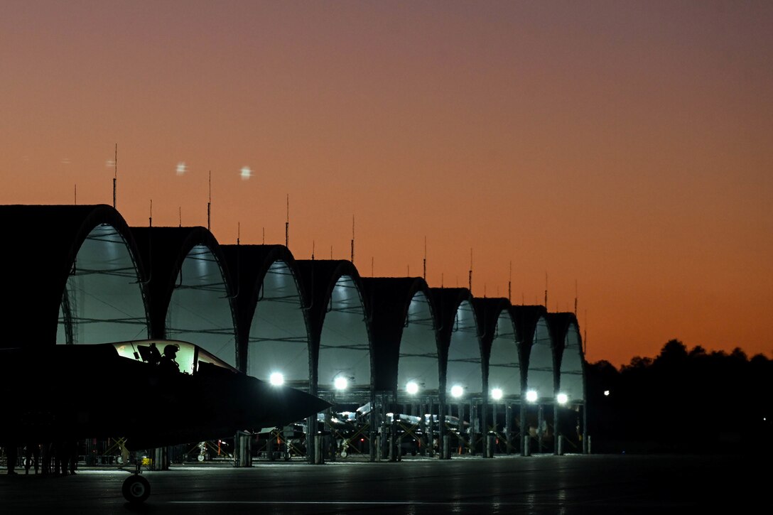 A military jet pulls out of a hangar at night.